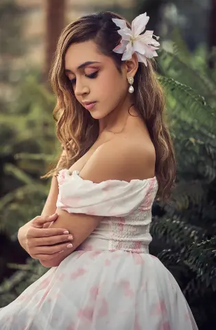 Dreamy portrait of a woman in a white floral off-the-shoulder dress posing in a lush green garden.