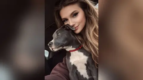 AnyaSin poses closely with her grey and white dog, resting her chin on its head while looking into the camera.