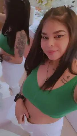 Young woman in a green tank top and white pants smiling in a bright indoor setting.