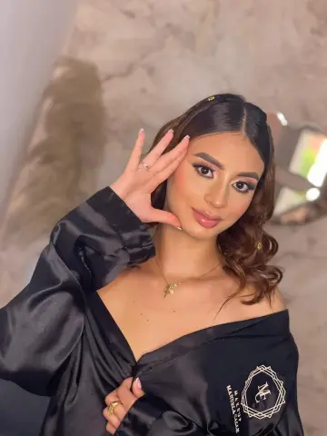 AbbyChannel poses with her hand near her face, wearing a black satin robe that shows her cleavage and shoulders.