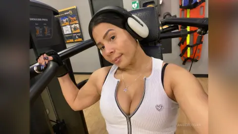 Smiling woman in white ribbed tank top wearing headphones during a gym workout session.