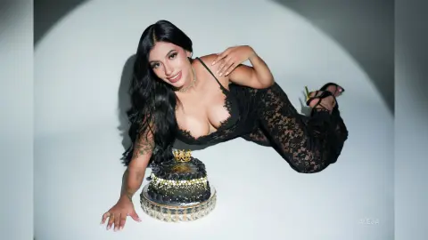 Aleja lies on a white floor wearing a black lace bodysuit next to a decorated black cake.