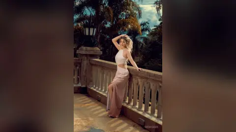 Elegant woman in a white cutout maxi dress posing on a stone balcony amidst lush tropical greenery.