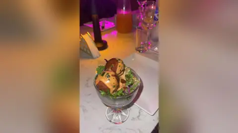 Gourmet appetizer dish with fried meatballs and greens served in a glass bowl on a marble restaurant table.