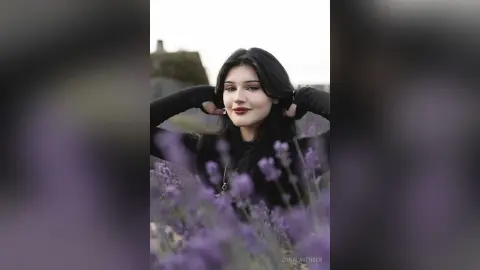 Young woman in a black outfit posing in a dreamy lavender field under soft natural light.