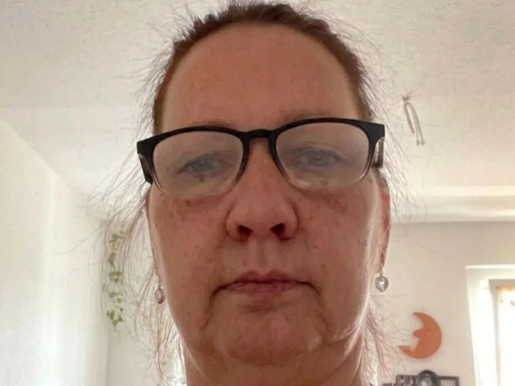 JosianeDelle — JosianeDelle looks directly into the camera wearing black-rimmed glasses with her hair pulled back.