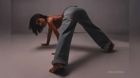 Fashionable woman in baggy denim jeans posing in a minimalist studio setting with moody lighting.