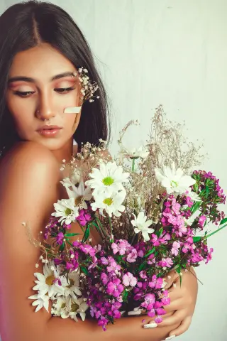 Young woman with floral hair accessory holding a bouquet of white and pink wildflowers in a dreamy setting.