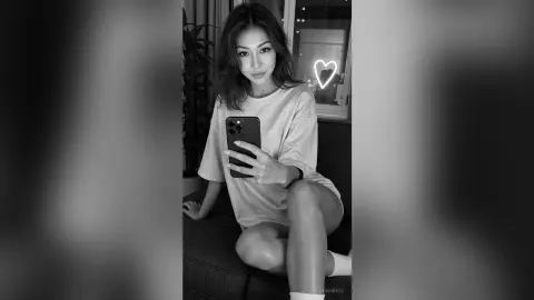 LeahReel — Young woman in a casual t-shirt taking a moody black and white selfie in a dimly lit room.
