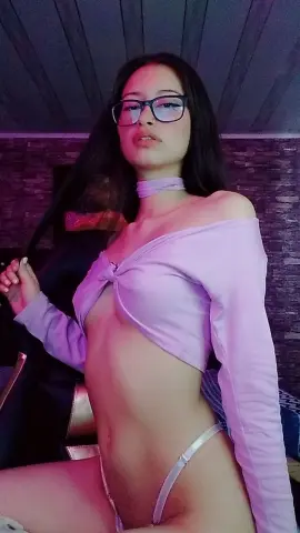 Young woman in a lavender off-the-shoulder crop top and choker posing in moody purple lighting.