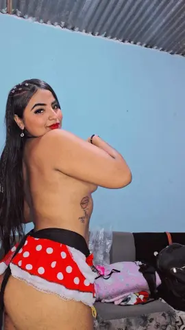 Smiling young woman with long dark hair wearing red polka dot ruffled shorts in a blue room.