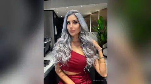 Glamorous woman with long wavy silver hair wearing a red crop top in a modern luxury interior.