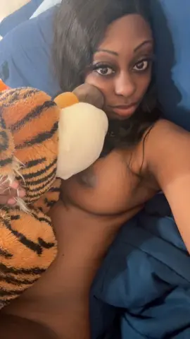 Young woman with long dark hair relaxing in bed with a tiger plushie in a cozy, intimate setting.