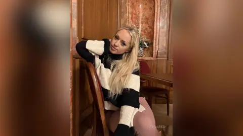 Blonde woman in a black and white striped turtleneck sweater relaxing in a classic wood-paneled room.