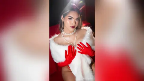 RosieThomas — Glamorous woman in a white faux fur outfit and red gloves posing in a moody, red-lit setting.
