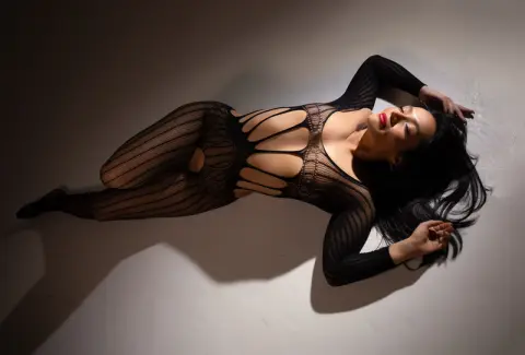 Elegant woman in a black cutout bodysuit lying on a white floor with dramatic studio lighting.