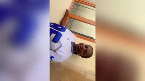 Shaluwah — Shaluwah wears a white jersey with blue numbers while leaning against a window frame indoors.