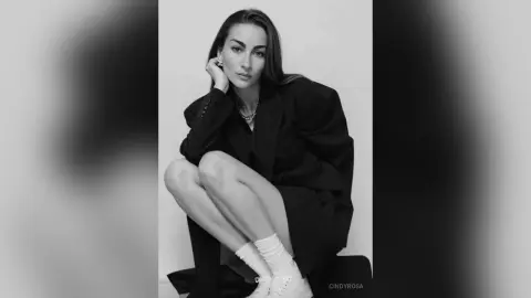 Elegant woman in a black oversized blazer and white socks posing in a minimalist studio setting.