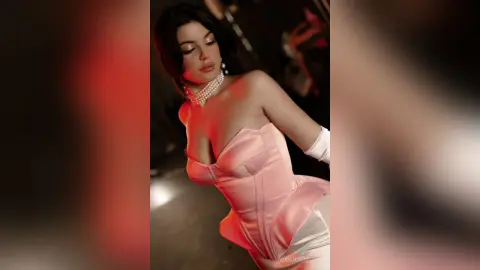 Elegant woman in a pink satin corset and white gloves posing in moody, dramatic studio lighting.