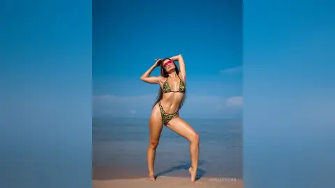 Slim woman in a leopard print bikini posing on a sunny tropical beach under a clear blue sky.