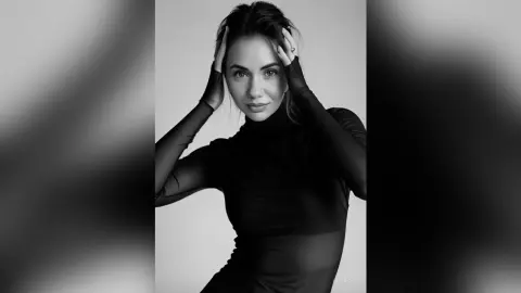 Elegant woman in a black turtleneck posing for a moody black and white studio portrait.