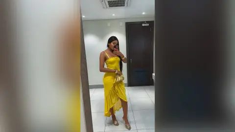 Elegant woman in a yellow satin midi dress posing in a mirror for a chic fashion selfie.