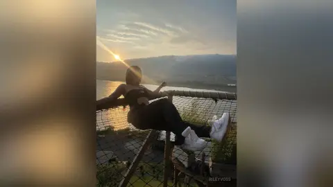 Young woman in black casual outfit relaxing on a net overlooking a scenic valley at sunset.