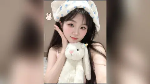 Young woman in cozy white pajamas and bunny hat holding a plush rabbit in a soft, dreamy indoor setting.