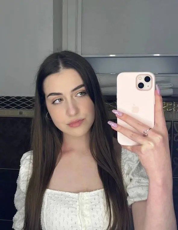SashaShin poses with long brown hair, wearing a black top and looking directly at the camera in a close-up shot.