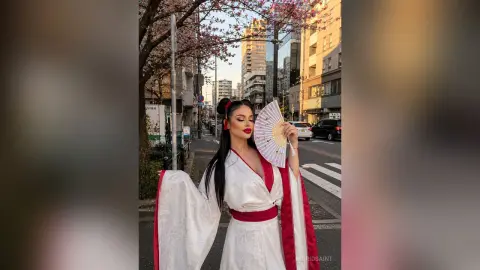 IngridSaint poses on a city street wearing a white and red kimono while holding a paper fan.