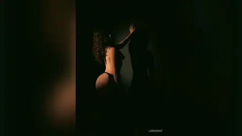 Moody silhouette of a woman in black lingerie posing in a dark, dramatic studio setting.