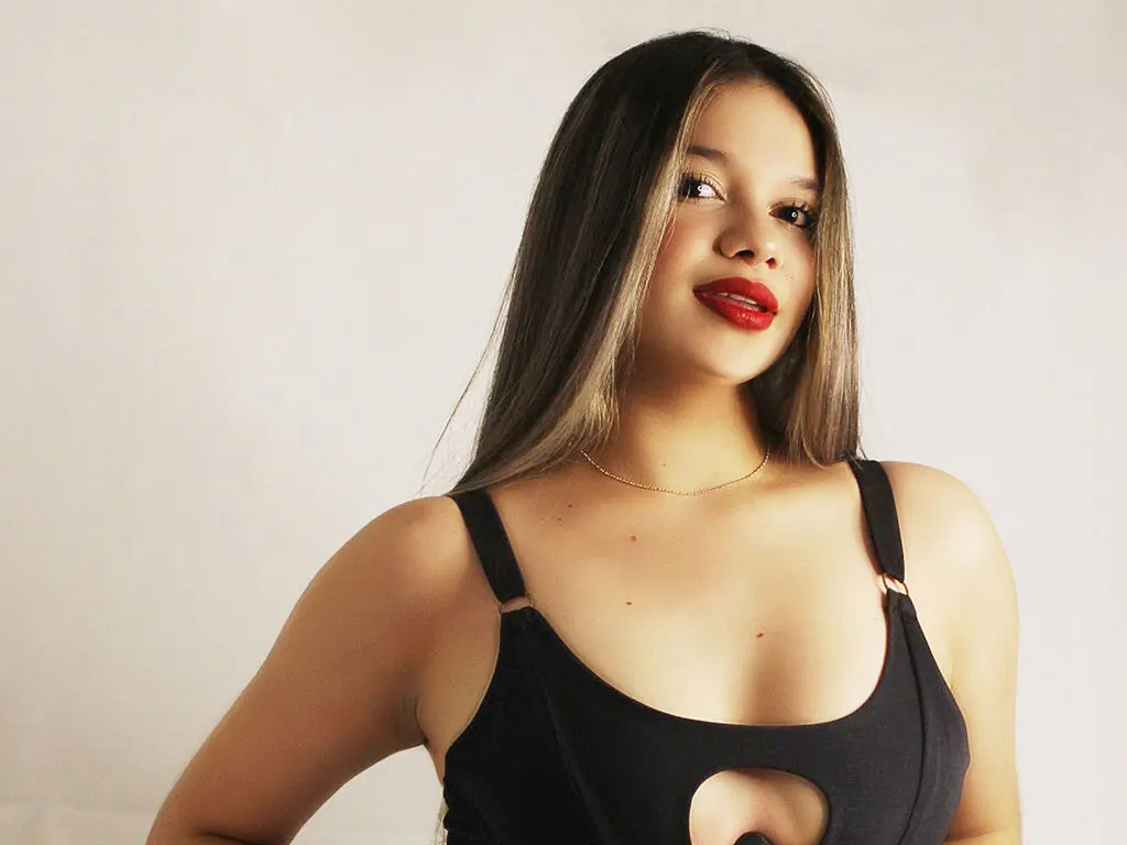 Young woman with long brown hair and red lipstick wearing a black tank top against a white background.