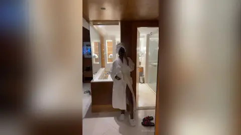 Woman in a white bathrobe and towel headwrap relaxing in a modern luxury hotel bathroom.