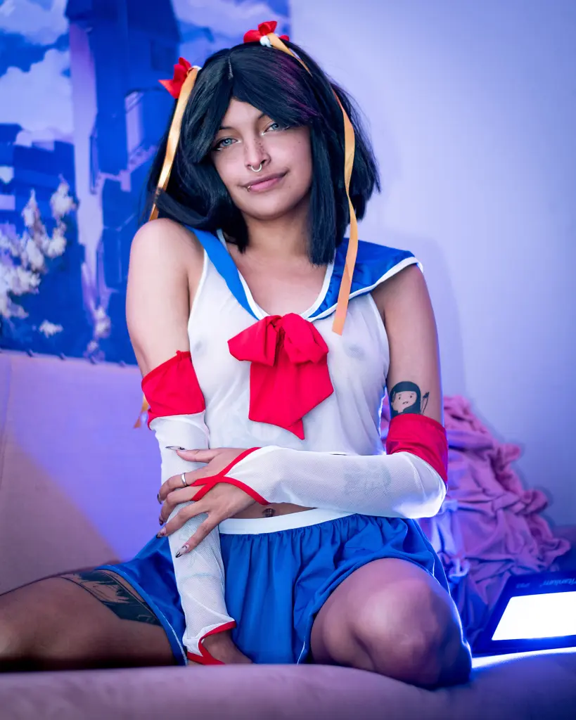 SakuraTao poses in a blue and white sailor-style outfit, showing her cleavage and shoulders with her black hair styled in a bob.