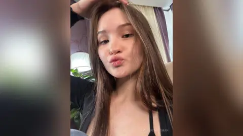 Young woman with long brown hair making a playful pouty face in a cozy indoor setting.