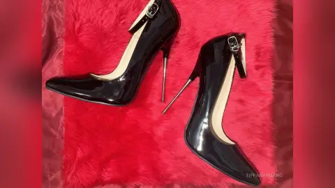 Elegant black patent leather stiletto high heels on a luxurious red faux fur background.