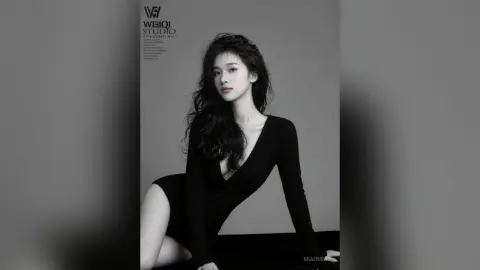 Elegant woman in a black long-sleeve bodysuit posing in a minimalist studio setting with a moody aesthetic.