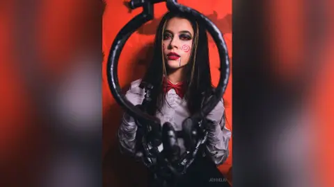 JessieLiu poses behind a black metal ring, wearing a white long-sleeved shirt and a red bow tie with red lipstick.