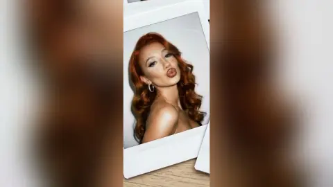 DeviNessa pouts her lips while posing in a close-up shot, showing her long wavy red hair and silver hoop earrings.