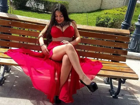 Alesya Nova — Alesya Nova sits on a wooden park bench wearing a long red dress and black high heels.