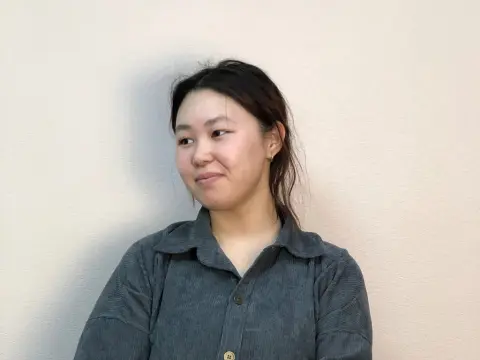 Willa Daggett — Willa Daggett wears a grey button-down shirt while looking to the side against a plain wall.