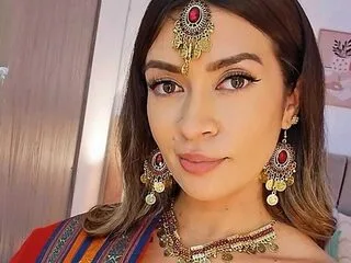 Victoria Romano — Victoria Romano looks directly at the camera wearing gold and ruby-encrusted jewelry and a patterned top.