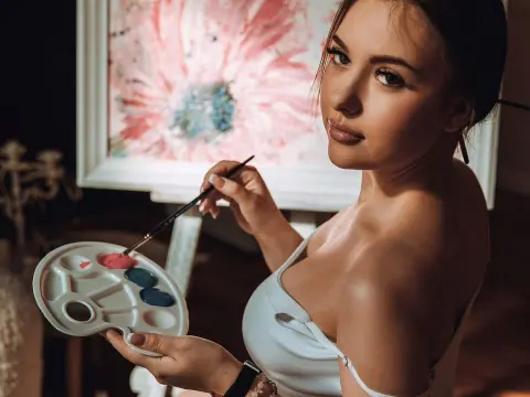 Lindsey Lu — Lindsey Lu holds a paint palette and brush while posing in a white top in front of a floral painting.
