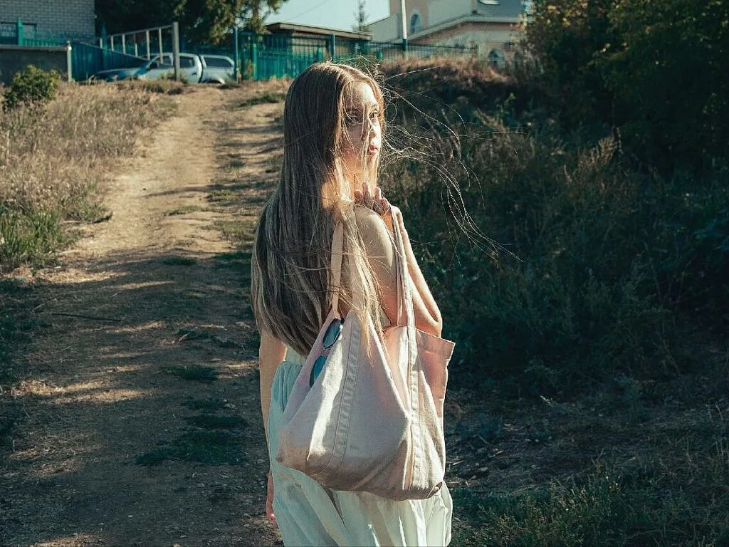 Karen Lowe looks back over her shoulder while walking down a dirt path with a large tote bag.