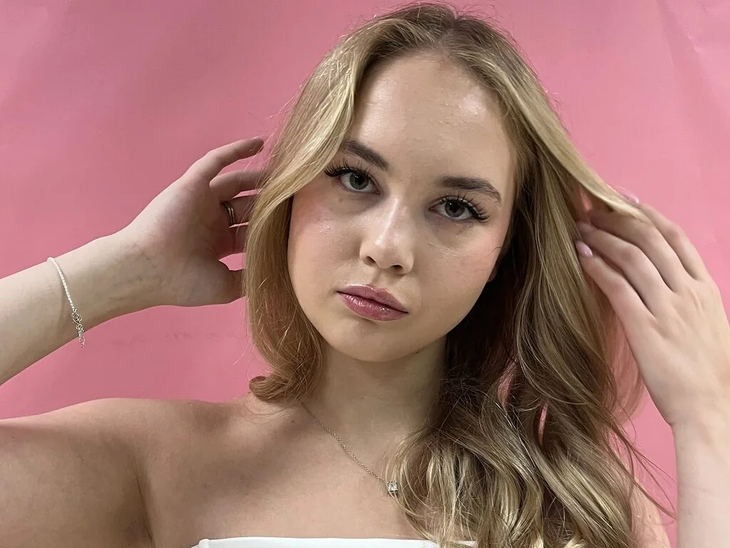 Shaquana Chappa poses with her hands in her blonde hair against a pink background.