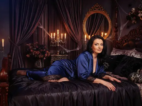 Lauren Newton — Lauren Newton lies on a dark bed wearing a blue satin robe with black lace trim.
