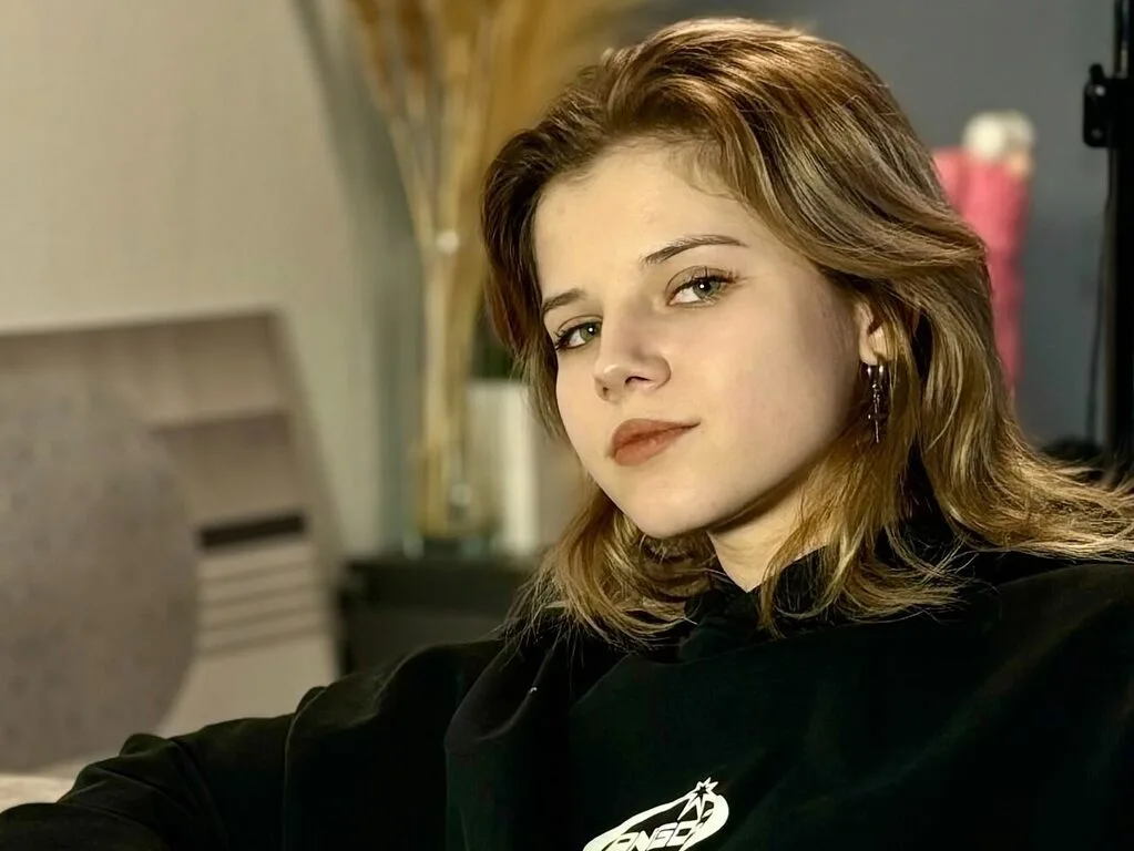 Machelle Fala looks toward the camera wearing a black hooded sweatshirt with her light brown hair styled down.