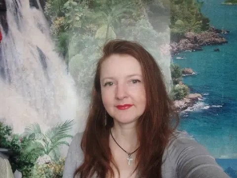 Megan Pirs — Megan Pirs smiles in a grey top and cross necklace against a tropical waterfall backdrop.