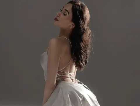 Ariel Evans — Ariel Evans poses in a white satin dress with thin straps against a grey background.
