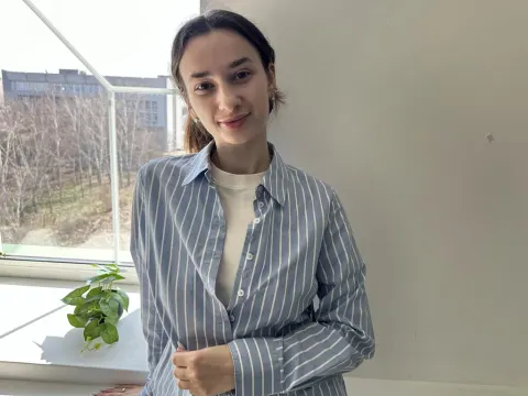 Jessica Breez — Jessica Breez smiles while wearing a blue and white striped button-down shirt over a white tank top by a window.
